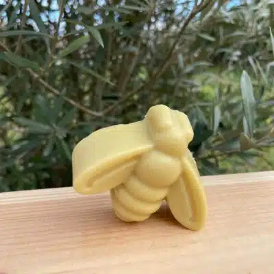 Savon en forme d'abeille, posé sur une planche en bois devant un petit olivier.