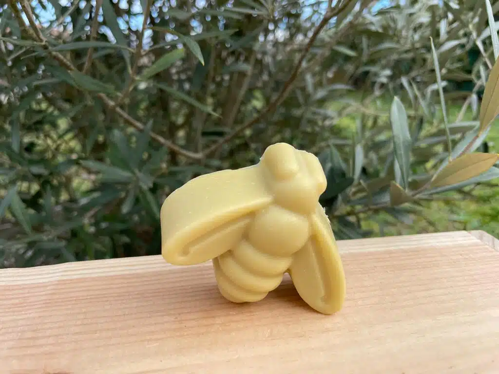 Savon en forme d'abeille, posé sur une planche en bois devant un petit olivier.