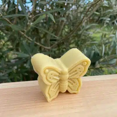 Savon en forme de papillon posé sur une planche en bois devant un petit olovier.
