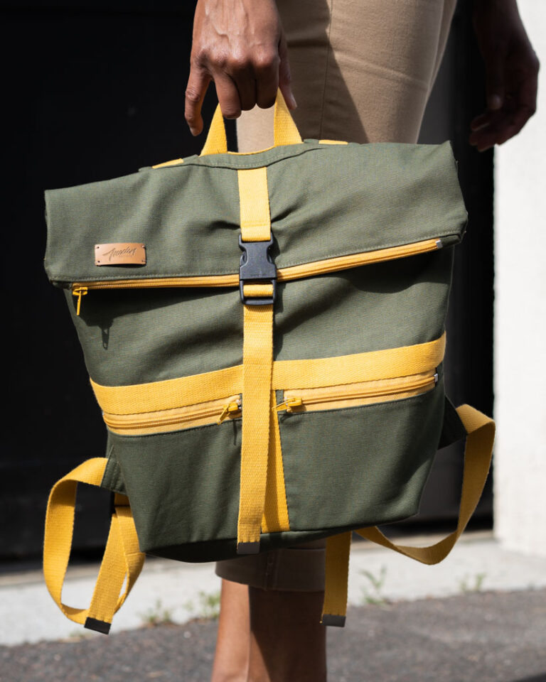 Sac à dos en tissu vert olive avec des accents jaune moutarde porté à la main