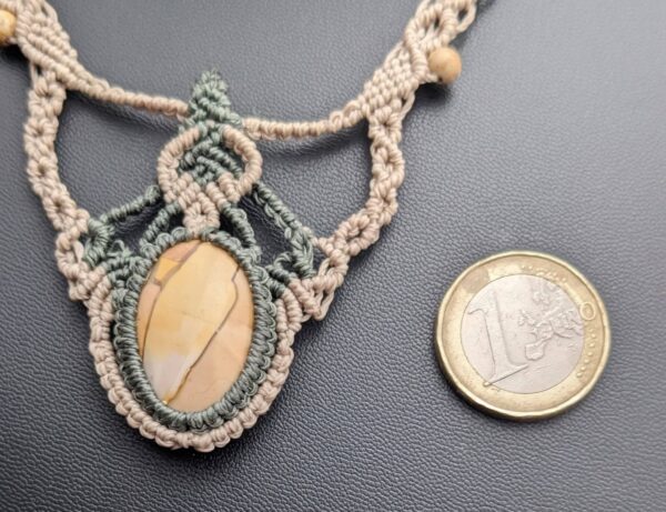 collier macramé beige et kaki a coté d une piece de 1 euro pour pouvoir comparer la taille