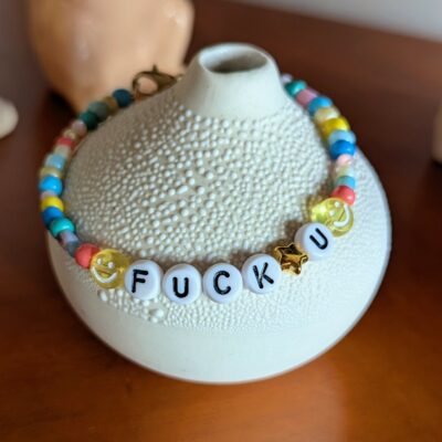 Bracelet en perles de rocaille multicolores avec fermoir . 2 smileys jaunes et les mots "fuck" et "u" séparés d'une petite étoile dorée.