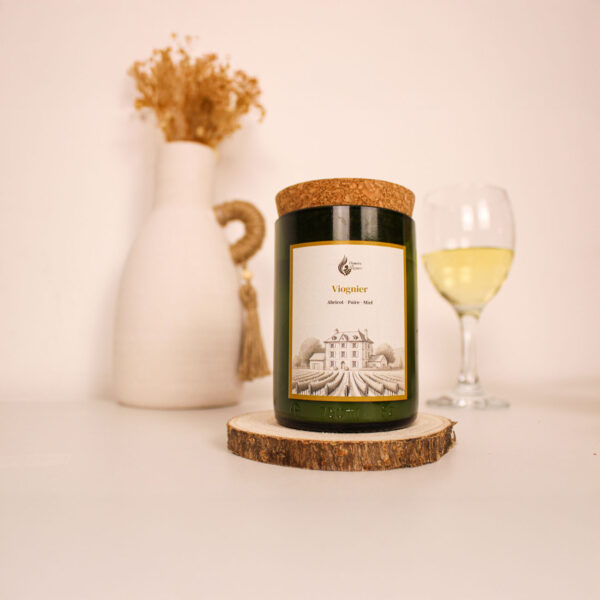 Bougie parfumée Viognier posée sur socle bois, vase déco et verre de vin en fond