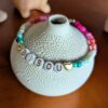 Bracelet en perles de rocailles en dégradé allant du bleu au rose avec 2 perles coeur, mot "bisou" écrit en perles plastique dorées. Avec fermoir argenté et chainette.