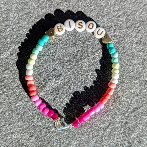 Bracelet minimaliste en perles de rocaille avec mot "bisou" dégradé allant du rose au bleu. Perles avec écriture dorée et fermoir ajustable.