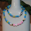Collier dans les tons de bleus et de jaune, en perles de rocaille fantaisie. Perles étoiles et écrit "BICHE" en lettres roses.