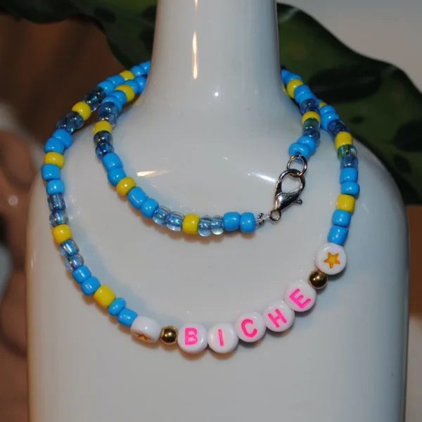 Collier dans les tons de bleus et de jaune, en perles de rocaille fantaisie. Perles étoiles et écrit "BICHE" en lettres roses.