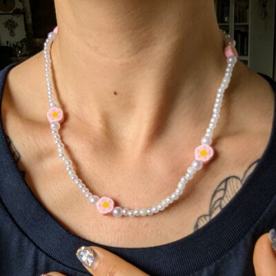 Collier fait main porté autour du cou, composé de perles nacrées blanches et de perles fleurs roses au cœur jaune, dans un style fairycore et délicat.