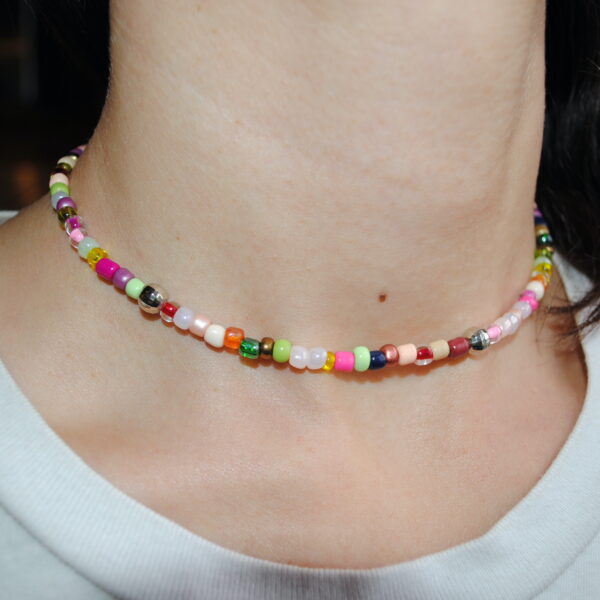 Ce ravissant ras de cou multicolore habille avec élégance le cou de la personne qui le porte, apportant une note de fantaisie et d’originalité à son allure. Il se compose d’un assemblage harmonieux de perles aux teintes éclatantes et pastel, mêlant du rose, du vert, du jaune, du bleu, du blanc et du rouge. Chaque perle, qu’elle soit en rocaille ou en plastique scintillant façon boule à facette, est agencée avec soin pour offrir un rendu à la fois ludique et tendance. Délicatement posé sur la peau, ce bijou souligne avec finesse le cou grâce à son design ajusté et minimaliste. Quelques perles métalliques viennent rehausser l’ensemble d’une touche subtile d’éclat et de modernité. Inspiré des tendances bohèmes et Y2K, ce ras de cou est le parfait accessoire pour sublimer une tenue estivale, apporter une touche fun à un look décontracté ou encore jouer sur l’accumulation avec d’autres colliers pour un effet plus sophistiqué.