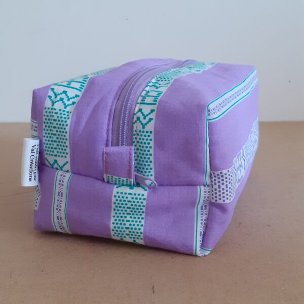 Trousse de toilette zippée, mauve avec de larges bandes blanches et motifs géométrique vert apposées sur celles ci.