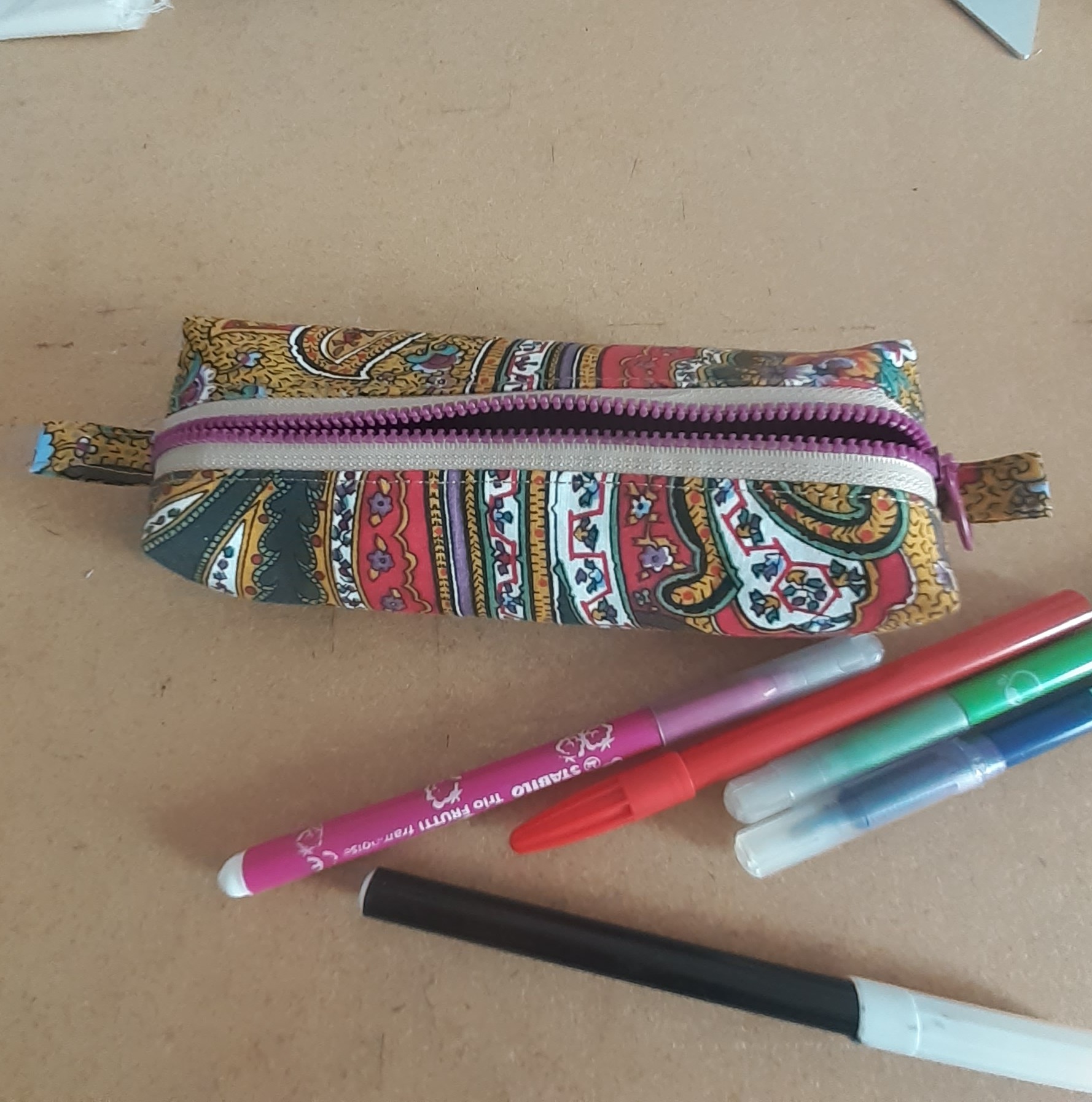 Trousse en tissu bleu avec motifs de feuilles roses et une fermeture à glissière turquoise.