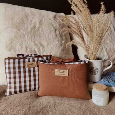 Duo de pochettes format poche en tissus chinés, posées sur un lit avec tasse et bougie.