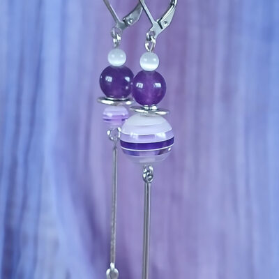 Boucles d’oreilles pendantes violettes au design asymétrique, composées de perles élégantes et de détails argentés. Un bijou raffiné qui apporte une touche chic et moderne à toutes vos tenues.