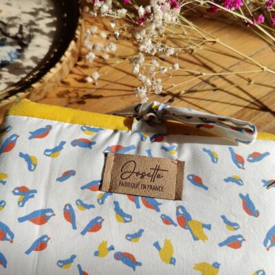 Détail du tissu upcyclé de la pochette, motif oiseaux colorés sur fond clair.