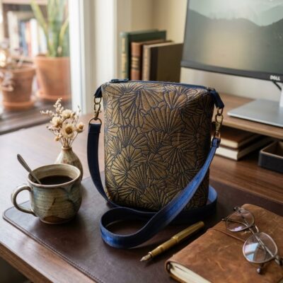 sur un bureau. Il est placé sur un sous-main en cuir brun, à côté d'une tasse de café en céramique artisanale, d'un stylo-plume et d'un carnet de notes ouvert, créant une ambiance professionnelle et organisée.