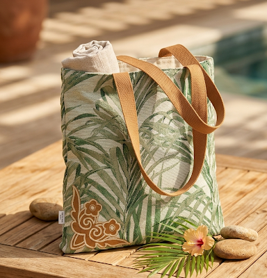 sac ou tote bag en tissu canva feuillage vert fond beige sable avec détail d'une broderie représentant des fleurs ocres cousue sur un angle en bas du sac. et ses anses en sergé de coton ocre. Posé sur une terasse au bord d'une piscine. dispensable pour une après-midi au bord de l'eau.