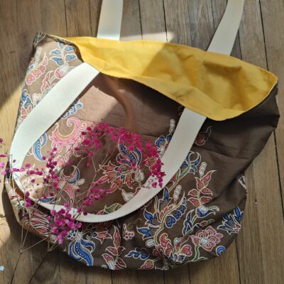 Tote bag upcyclé aux motifs floraux colorés et intérieur jaune moutarde, posé sur un sol en bois clair, décoré d’une branche de gypsophile rose.