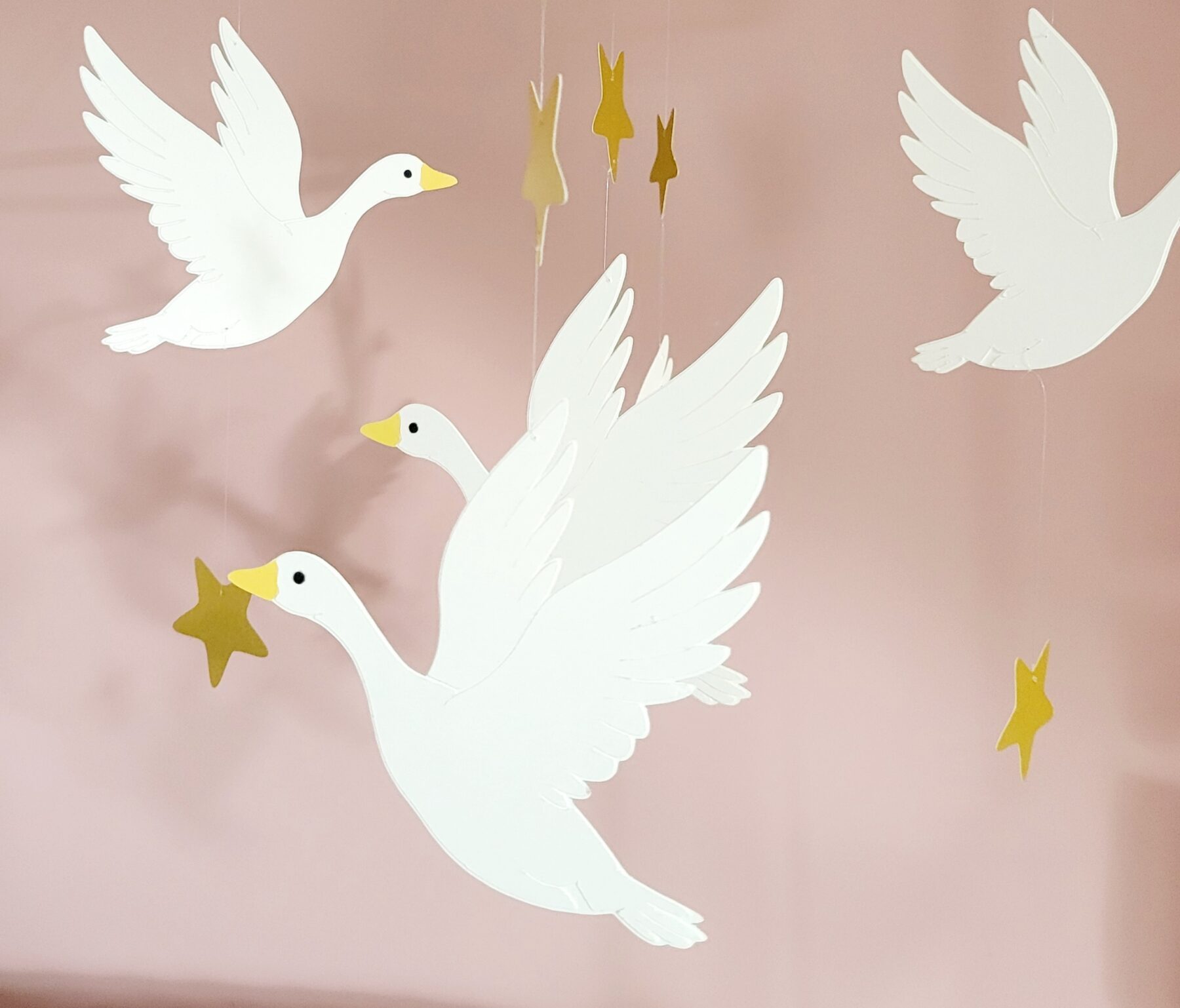 Décoration de chambre de bébé avec un mobile artisanal d'oies blanches en plein envol.
