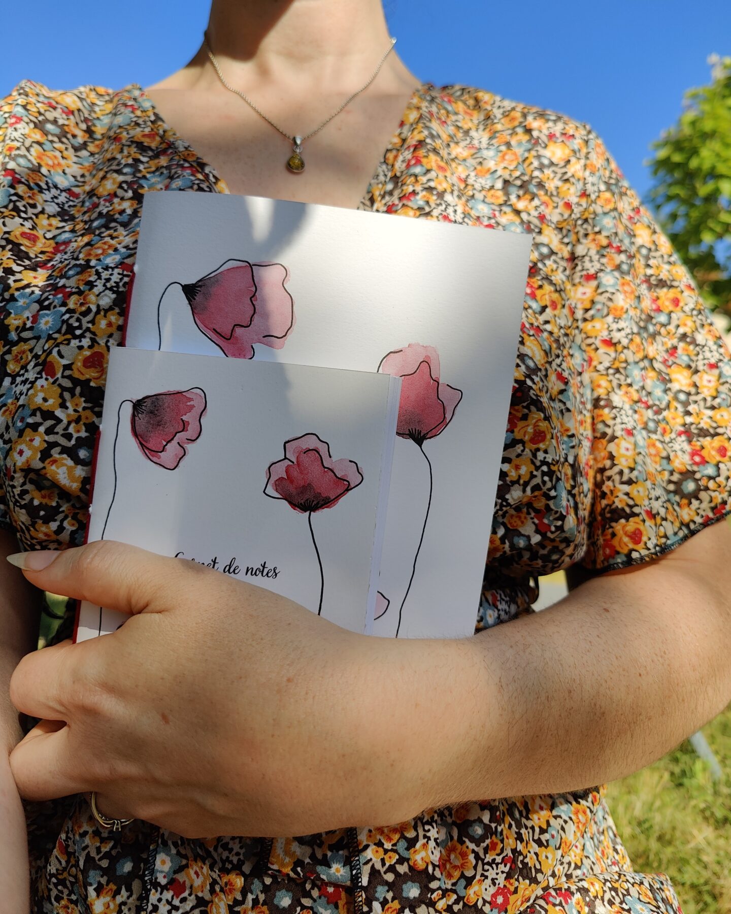 Une personne tenant deux carnets de notes A5 et A6 avec une couverture illustrée de coquelicots peints à l'aquarelle.