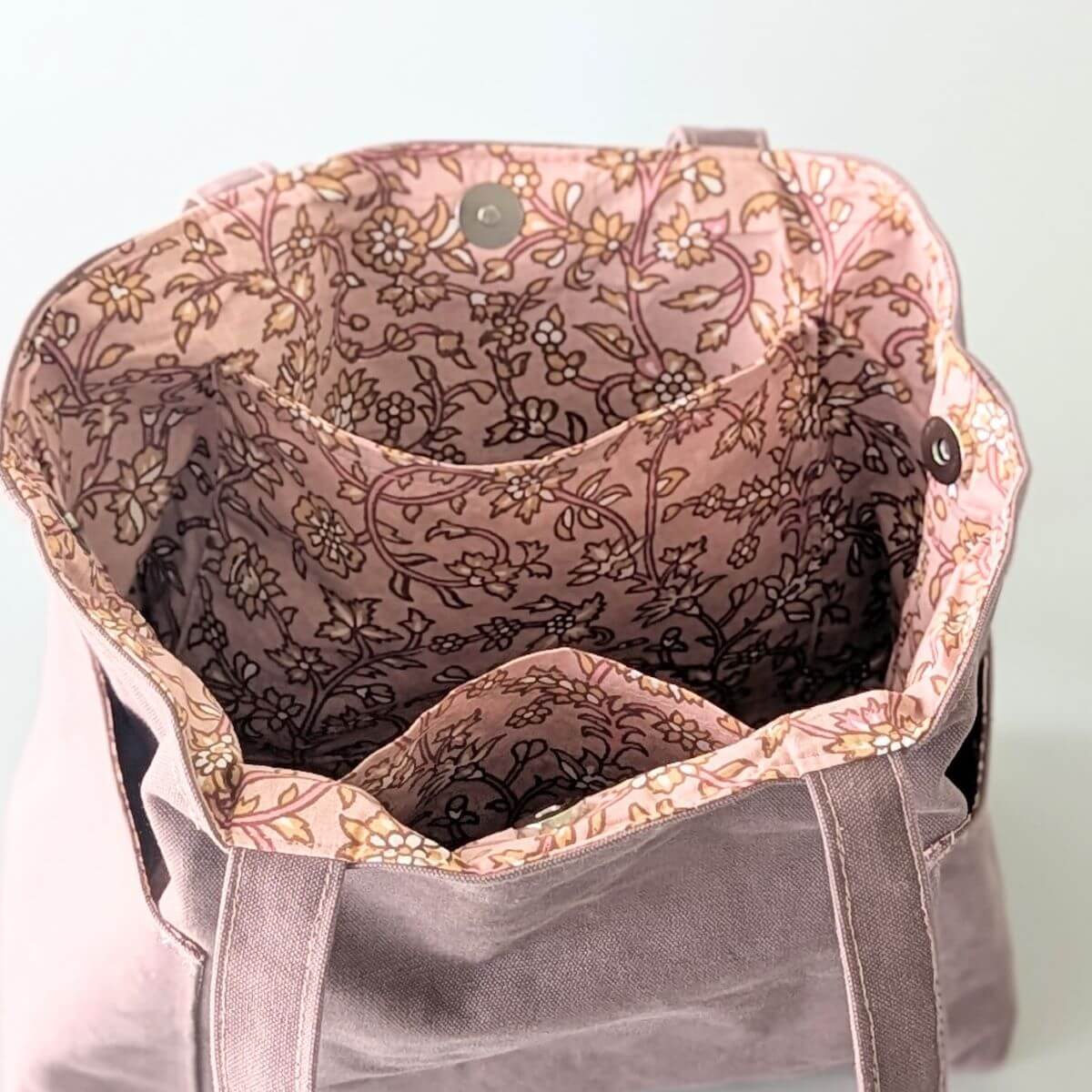 L'intérieur du sac trapèze montrant sa doublure fleurie aux tons roses, ses poches et ses boutons aimantés.