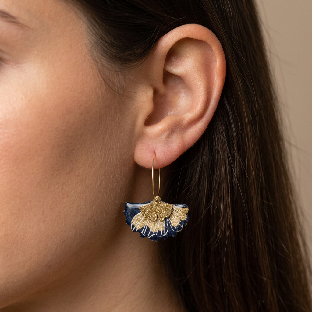 Créoles gingko bleu nuit et or portées à l'oreille, bijou fait main