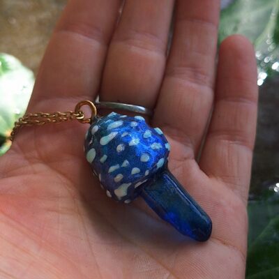 Collier pendentif unique en forme de champignon magique sculpté à la main, combinant art et nature pour un style fantastique et féerique. Pendentif champignon 4 x 5 cm, chaîne en acier inoxydable de 45 cm Cristal de quartz teinté, argile polymère, résine époxy, acier inoxydable Bleu vibrant avec des touches de blanc et nuances profondes Boîte cadeau soignée et prête à offrir Pendentif luminescent qui s'illumine dans le noir après exposition à la lumière, fait main en France Cottagecore, goblincore, fairycore, witchy, alternatif, fantastique, bohème, mystique